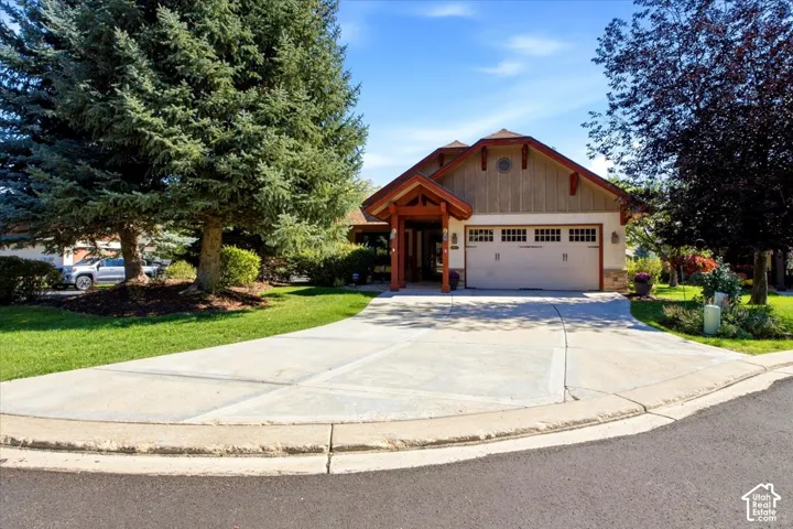 Front of home featuring an attached two-car garage, spacious concrete driveway, and mature trees