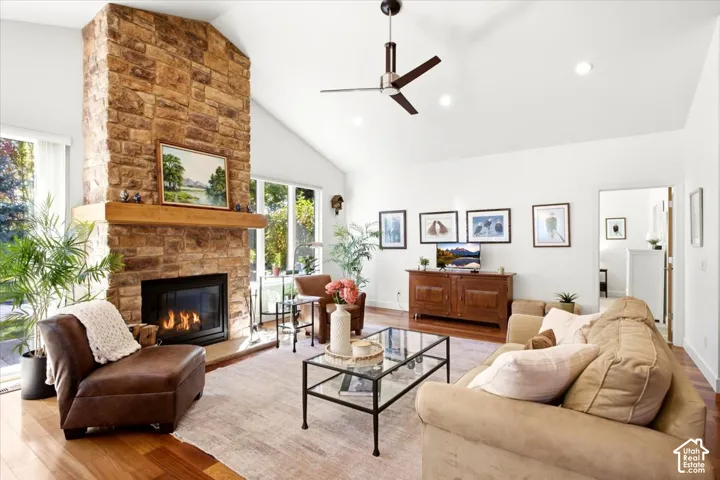 Living room featuring a Vaulted ceiling, stone fireplace with hearth, wood-finish flooring, and expansive windows