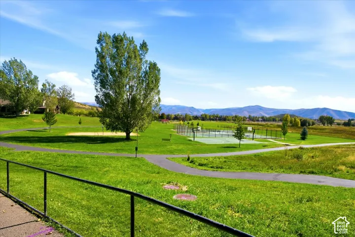 Expansive green space featuring a paved path, mature trees, and a multi-sport court