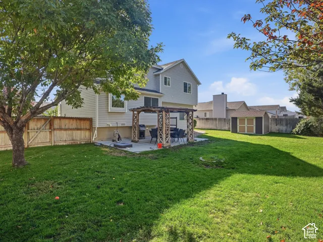 Expansive backyard featuring a concrete patio, a wooden pergola, a storage shed, and a privacy fence