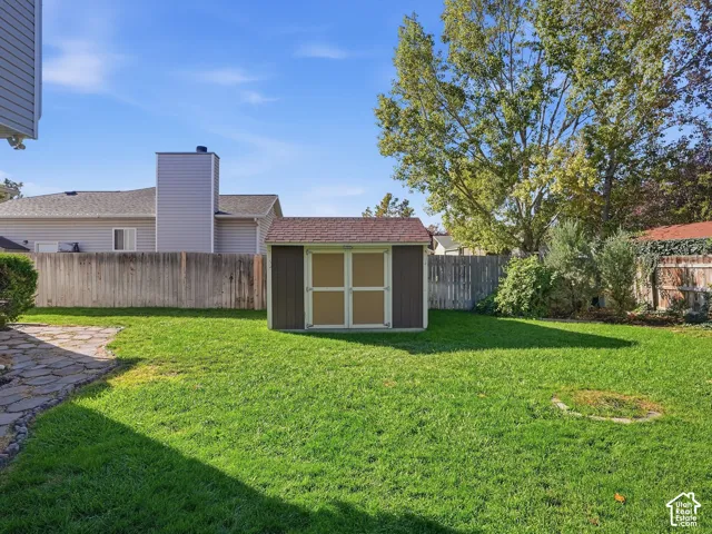 Expansive grassy yard with a storage shed, stone-patterned walkway, and perimeter fencing