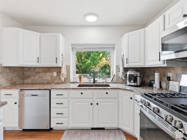 White cabinetry, stainless steel appliances, stone-look countertops, tiled backsplash, and a large window