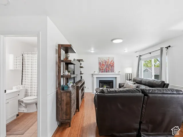 Hardwood-finish flooring, built-in media shelving, fireplace with mantel, white window trim, and a full bathroom with a single vanity