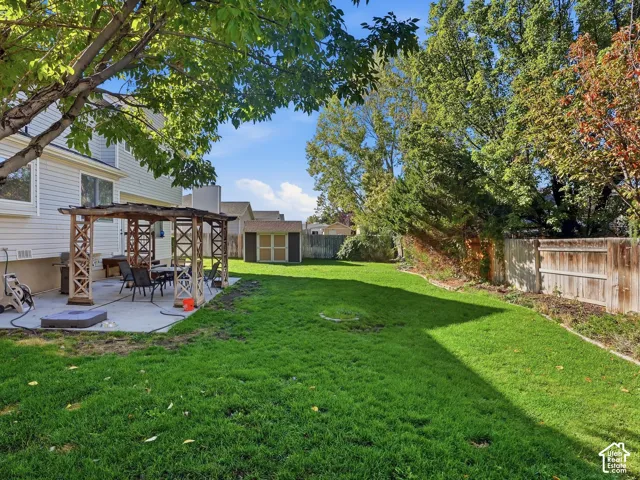 Expansive backyard featuring a large concrete patio, a wooden pergola, and a storage shed