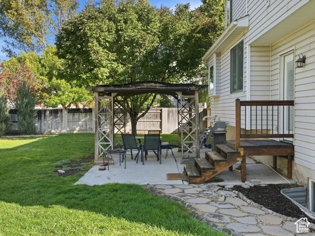 Expansive grassy yard featuring a concrete patio, wooden gazebo, and stone pathway