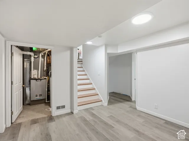 Wood-finish flooring with white baseboards, visible utility area, and a staircase with wood treads