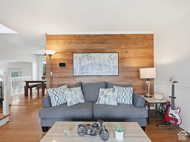 Wood-finish accent wall, wood-finish flooring, white crown molding, white painted railing, and a skylight