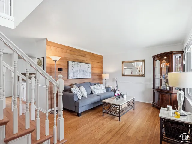Hardwood flooring throughout, wood-paneled accent wall, white wainscoting, and white crown molding