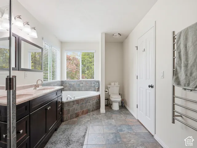 Dual vanity with dark wood-finish cabinetry, corner soaking tub with tiled surround, and slate-style floor tiling