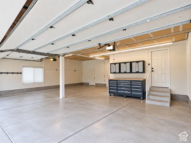 Spacious garage with concrete flooring, automatic garage door, built-in storage cabinetry, and a service door