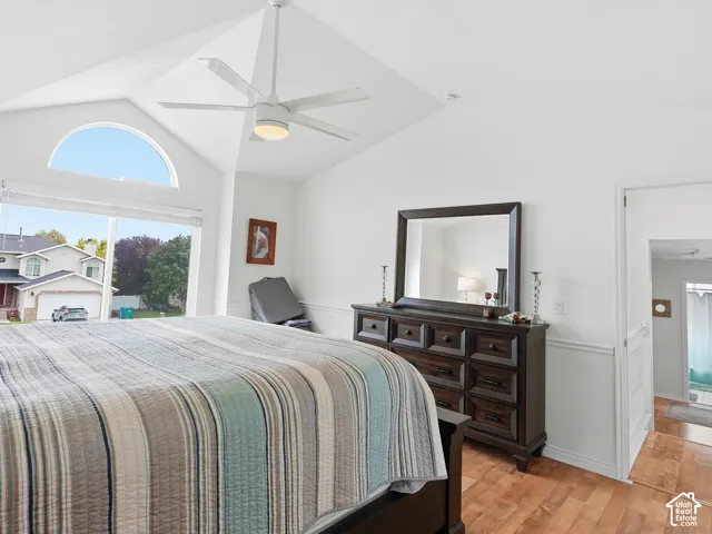 Vaulted ceiling with a contemporary ceiling fan, large window with an arched transom, wood-finish flooring, and white paneled walls