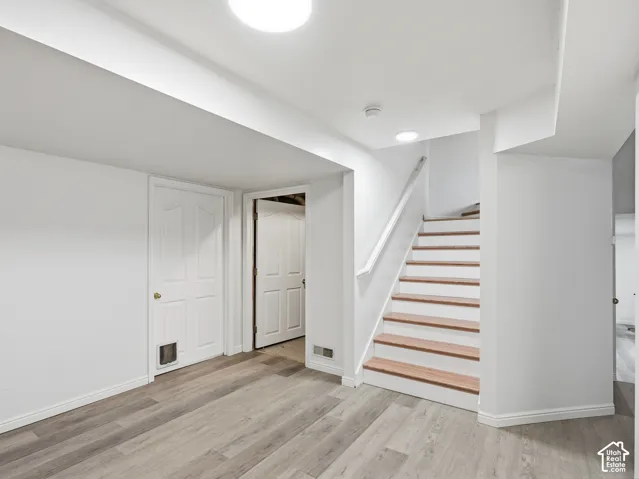 Wood-finish flooring, white painted walls, white interior doors, and a staircase with wood treads and white risers