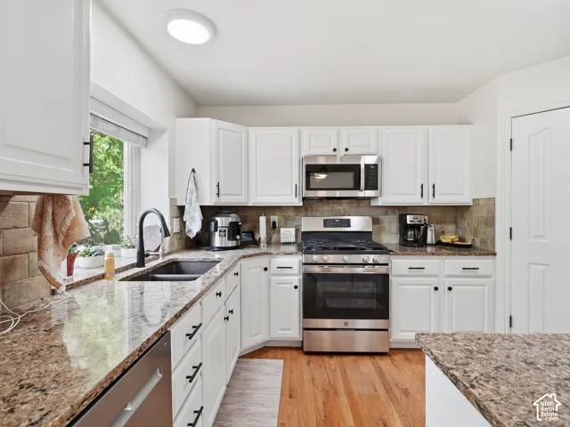 White cabinetry with dark hardware, stone countertops, stainless steel appliances, tile backsplash, and wood-finish flooring