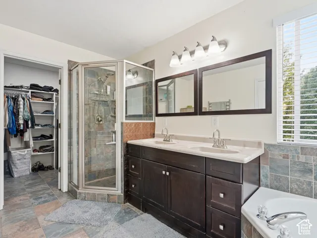 Dual sink vanity with dark wood-finish cabinetry, a glass-enclosed shower, built-in shelving in the closet, and multi-toned tile flooring