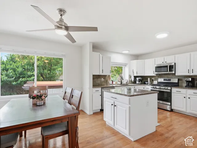 Kitchen featuring a central island with granite countertop, white cabinetry with dark hardware, stainless steel appliances, and a tile backsplash