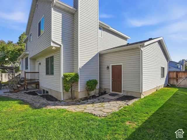 Light-colored siding exterior, wood deck, stone-finish pathway, brown door, and green lawn