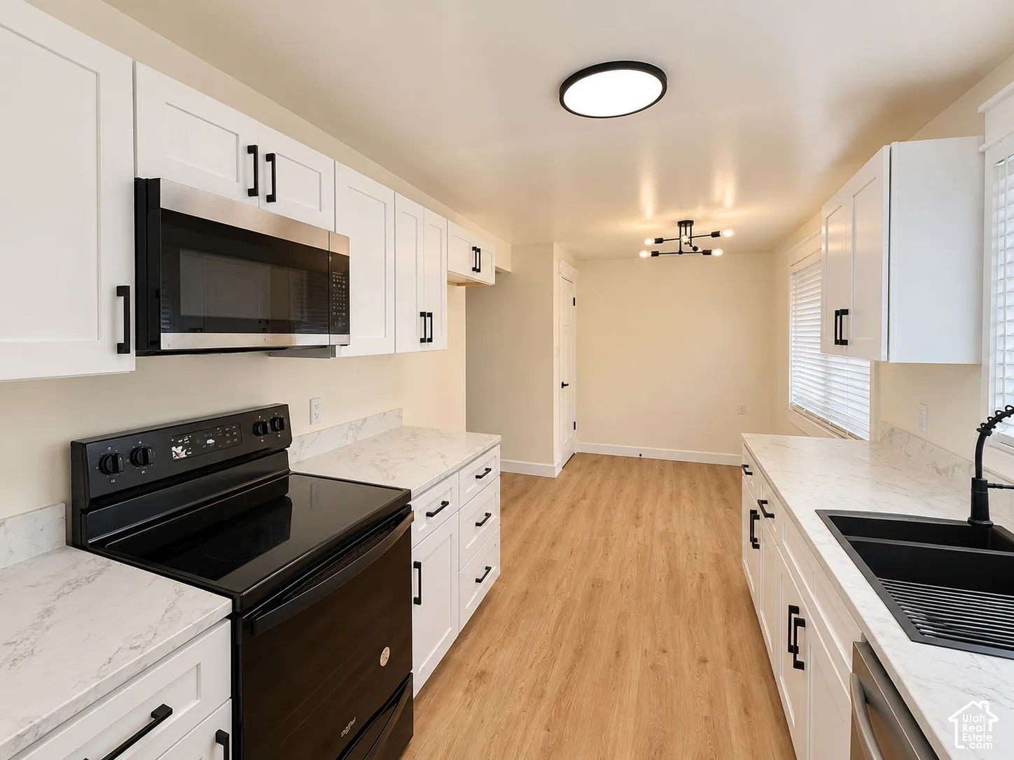 White shaker cabinetry with black hardware, white countertops, stainless steel microwave, black electric range, and wood-finish flooring