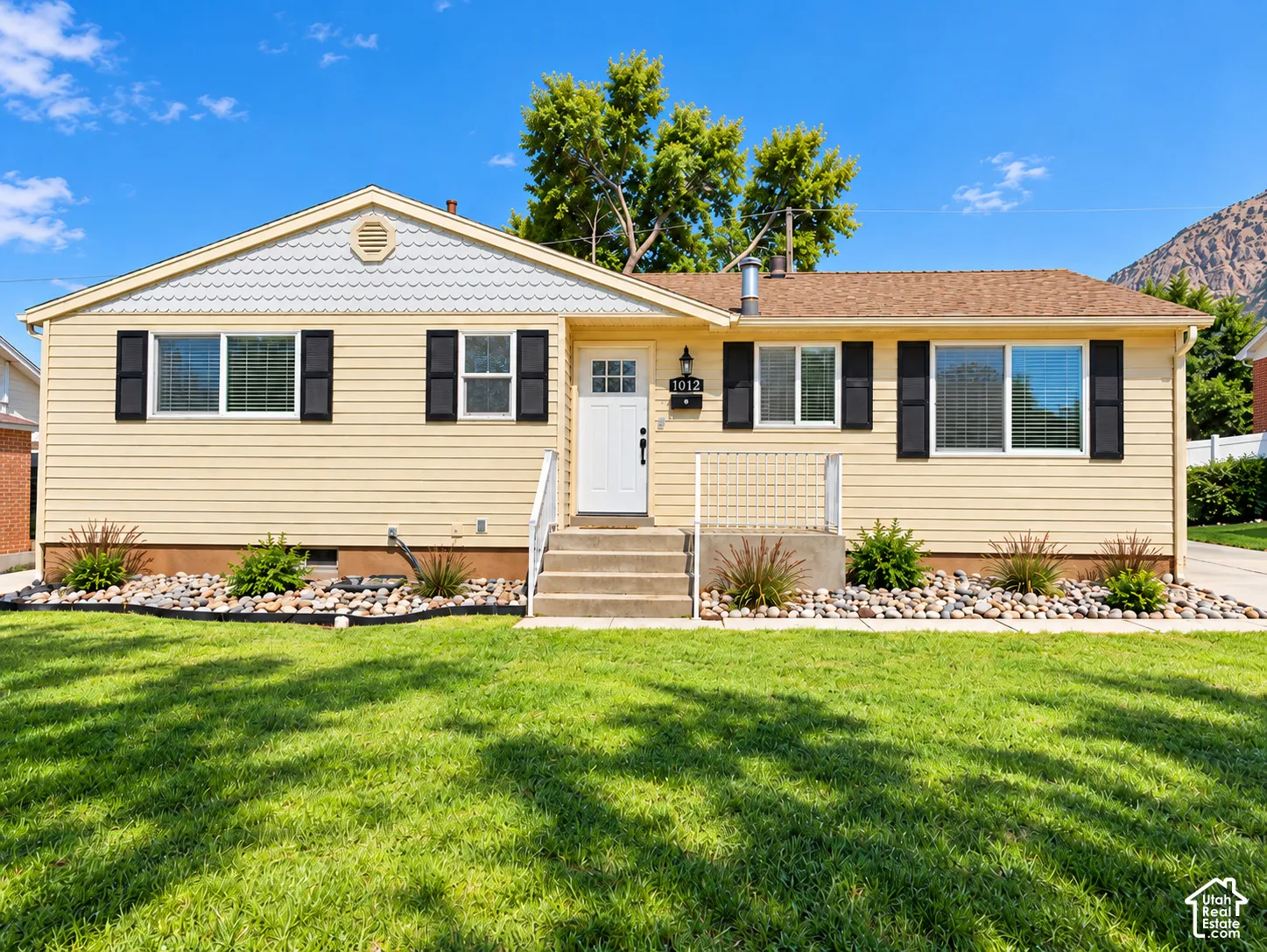 Single-story residence featuring light yellow siding, a white front door, and dark window shutters
