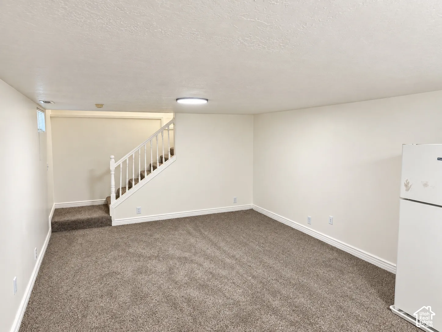 Carpeted flooring, white painted walls, white trim, white staircase with balusters, and a compact window