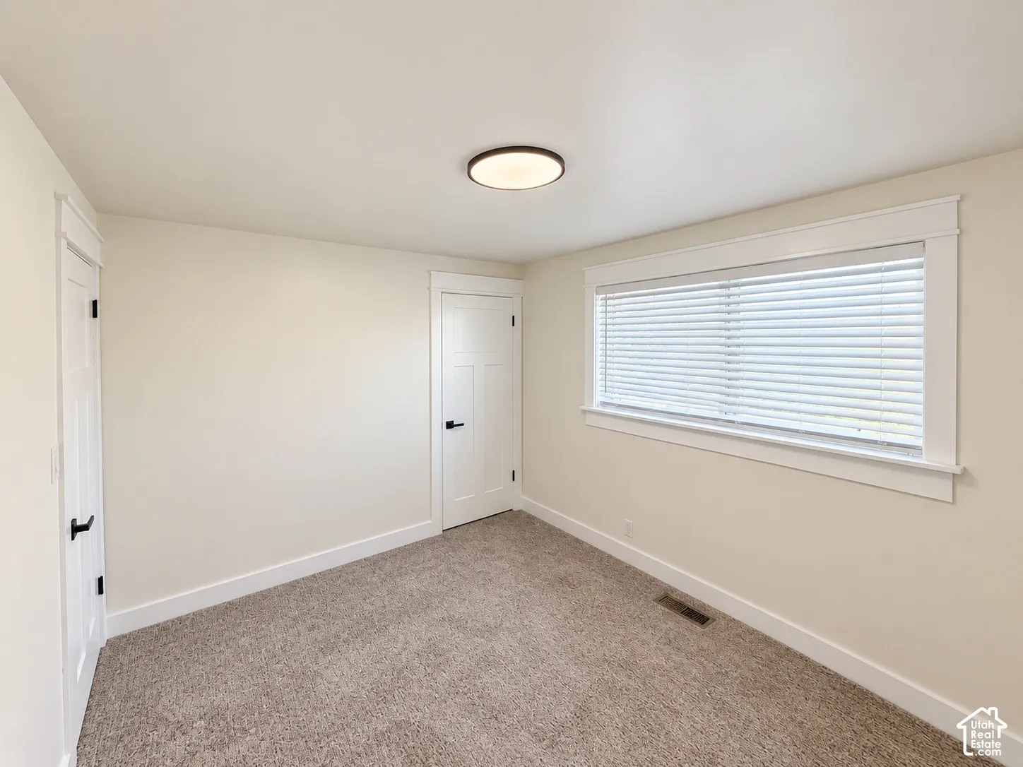 Neutral wall color, light-colored carpeting, white trim, recessed lighting, and a window with blinds