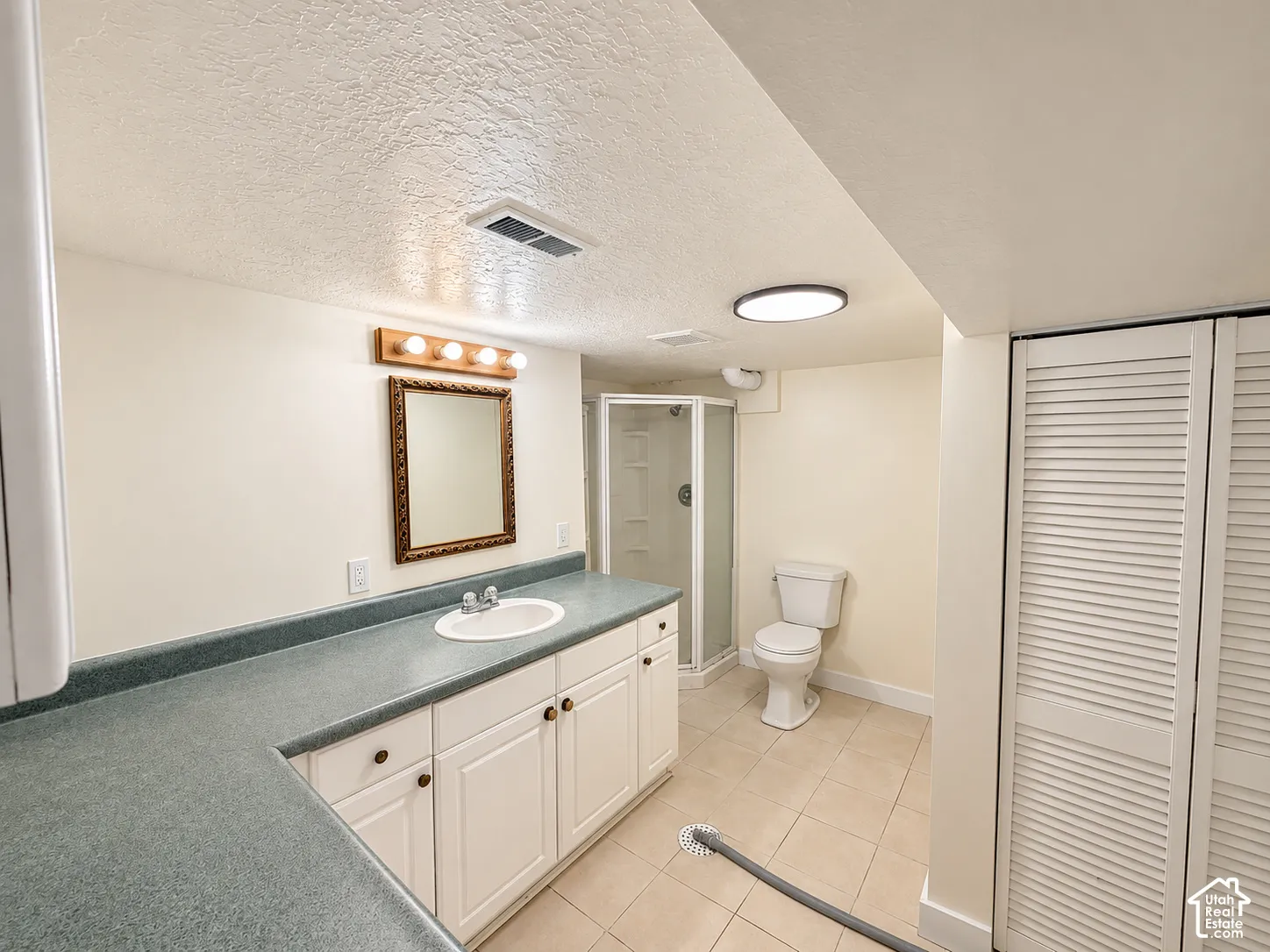 Expansive vanity with white cabinetry and a surface-mount sink, tiled flooring, a shower enclosure, and louvered bifold closet doors