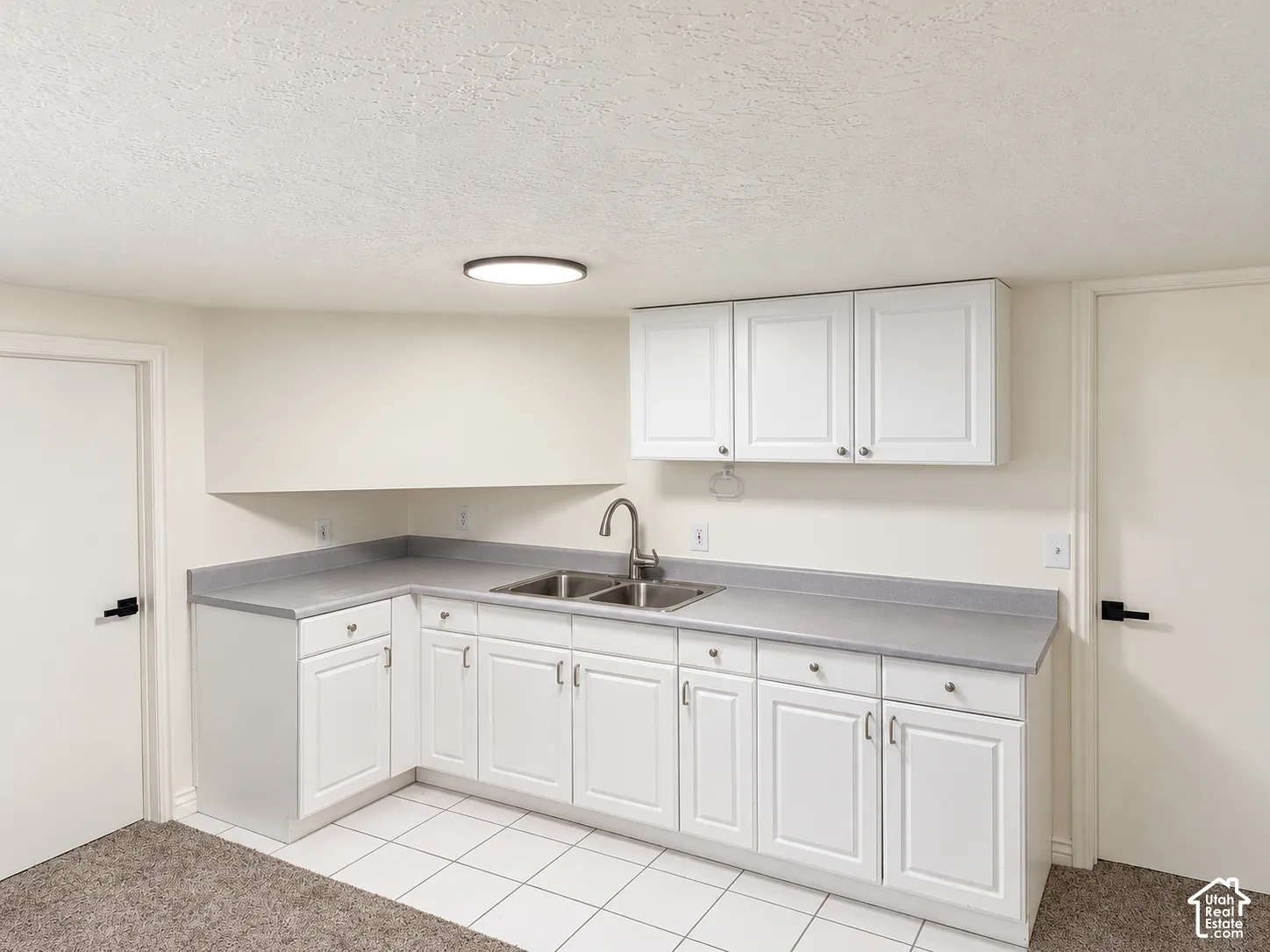 Functional kitchen area featuring white cabinetry, a dual basin stainless steel sink, and light gray countertops