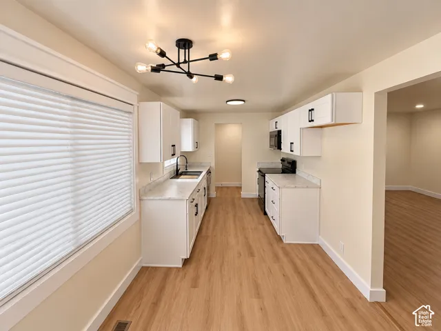 Galley kitchen featuring white cabinetry, light-toned countertops, wood-finish flooring, and a contemporary ceiling fixture