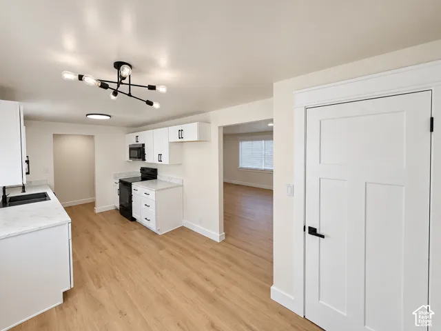 White cabinetry with matte black hardware, stone-finish countertops, black sink, and wood-finish flooring