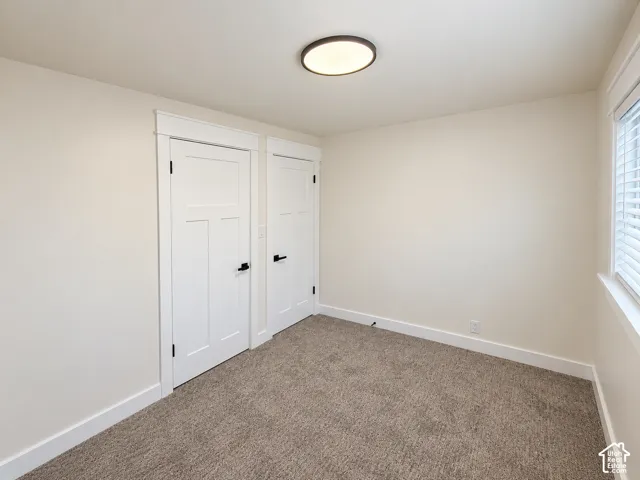 Neutral-toned walls, plush carpet flooring, white paneled doors, black door hardware, flush-mount ceiling light fixture, and a window with white blinds