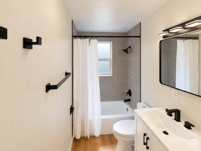 Bathroom featuring a white vanity with integrated sink, black fixtures, tiled shower surround, and wood-finish flooring