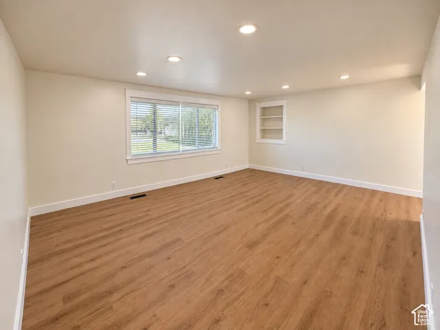 Spacious room featuring wood-finish flooring, recessed lighting, a large window with blinds, and built-in shelving