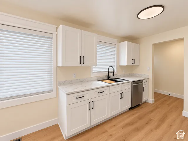 White shaker-style cabinetry with matte black hardware, light-toned countertops, stainless steel dishwasher, and wood-finish flooring
