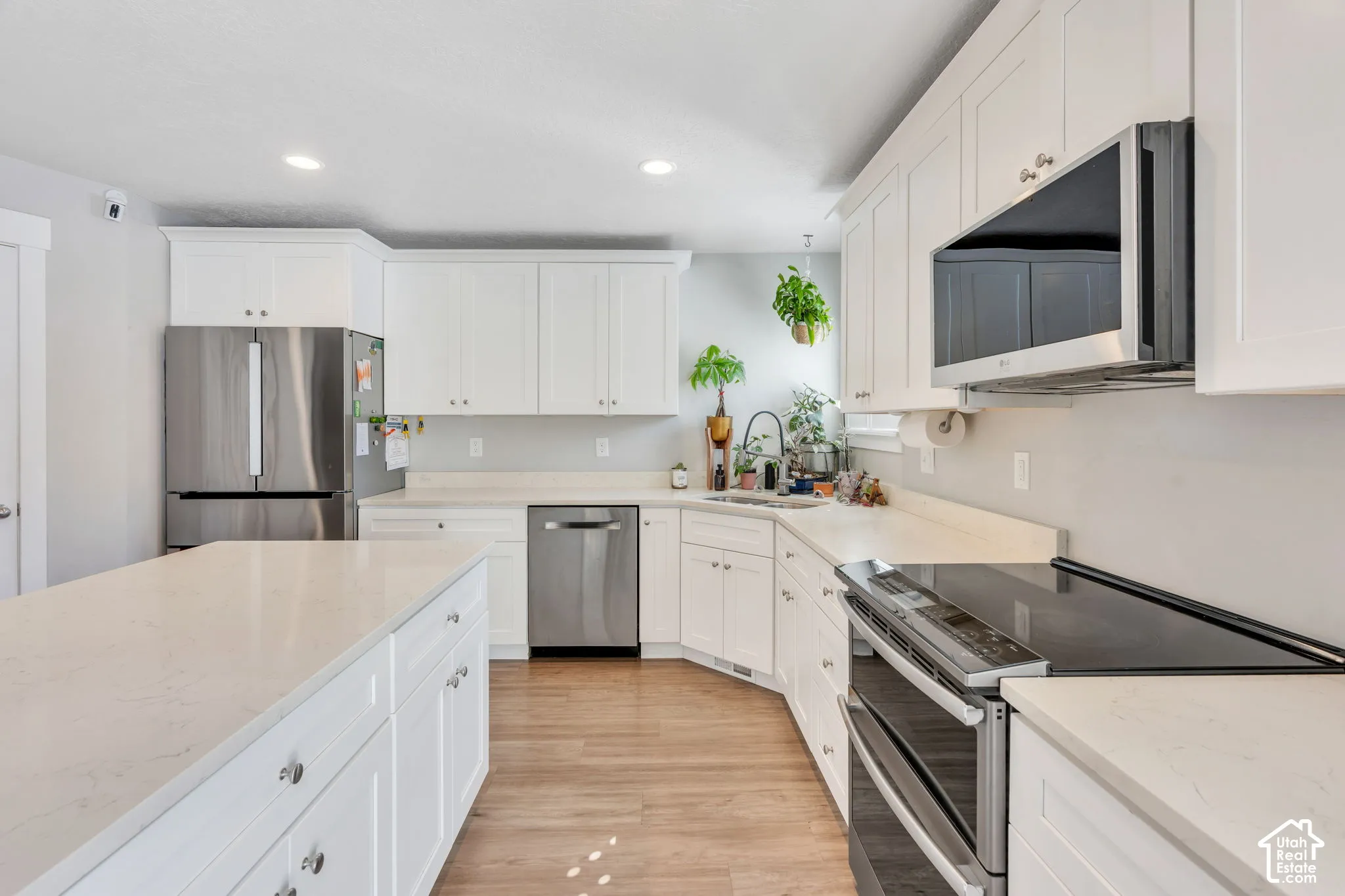 Kitchen featuring white cabinetry, light-toned countertops, stainless steel appliances, and wood-finish flooring