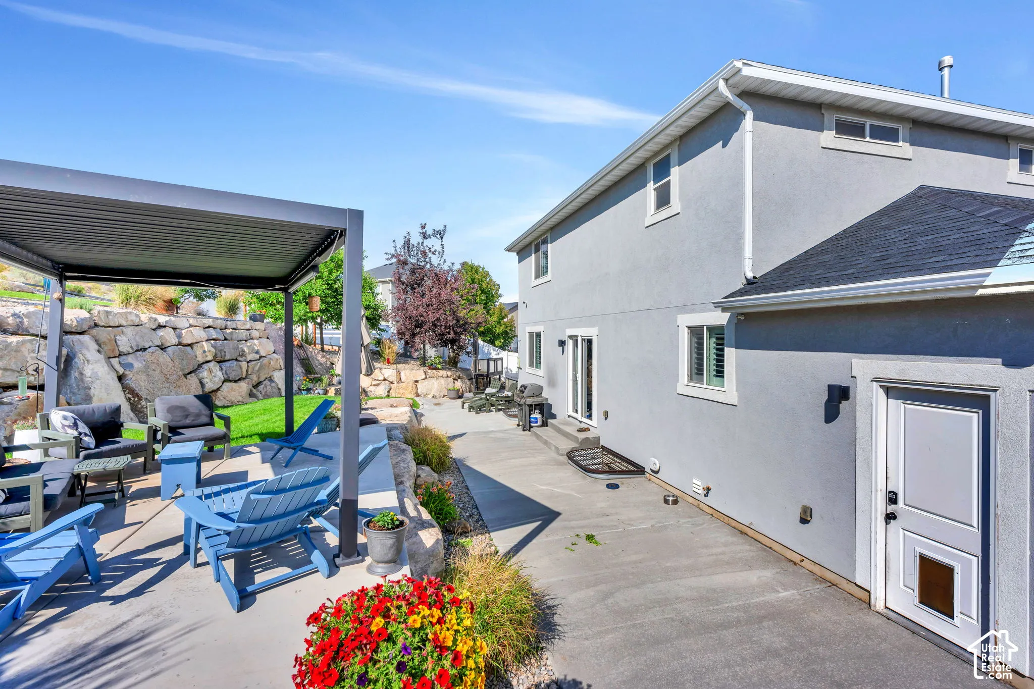 Outdoor patio with a modern pergola, a stucco exterior, multiple windows, and a paved walkway