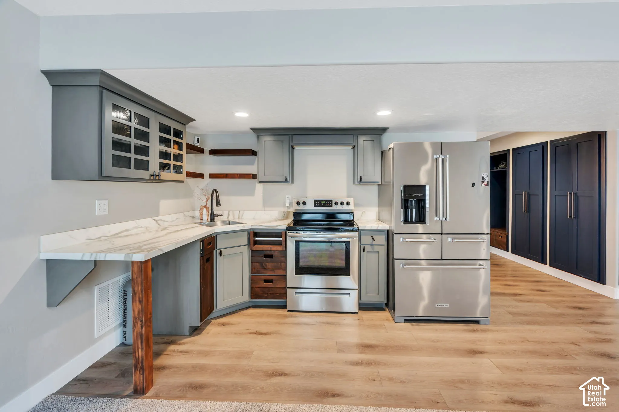 Kitchen featuring grey cabinetry with glass inserts, stainless steel appliances, a built-in wine rack, and wood-finish flooring