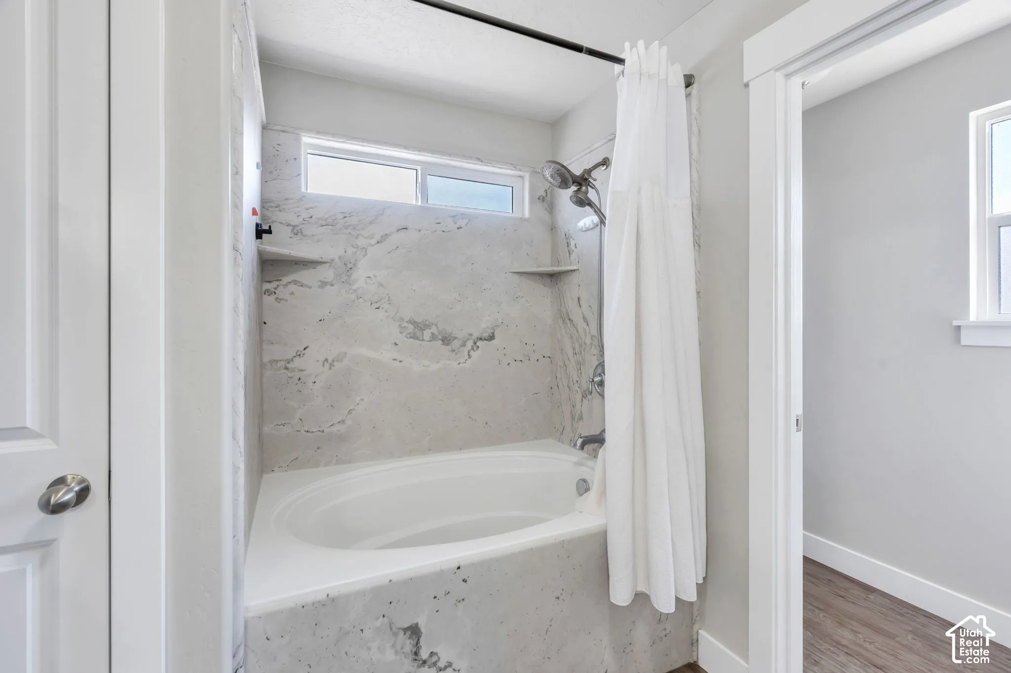 Alcove bathtub with a wall-mounted shower fixture, tiled surround, and integrated shelving