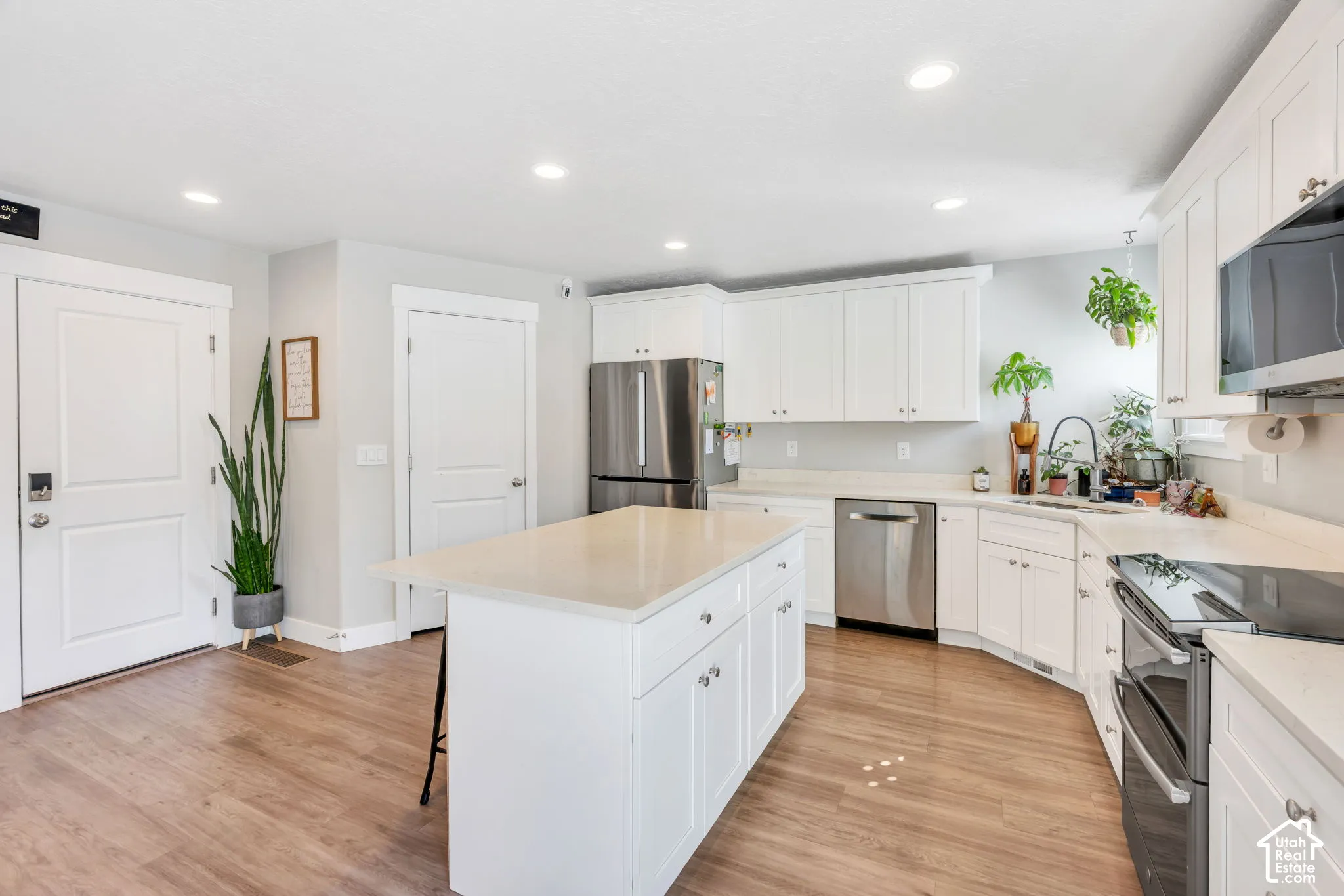 Modern kitchen featuring wood-finish flooring, white cabinetry, a center island with a light-toned countertop, and stainless steel appliances
