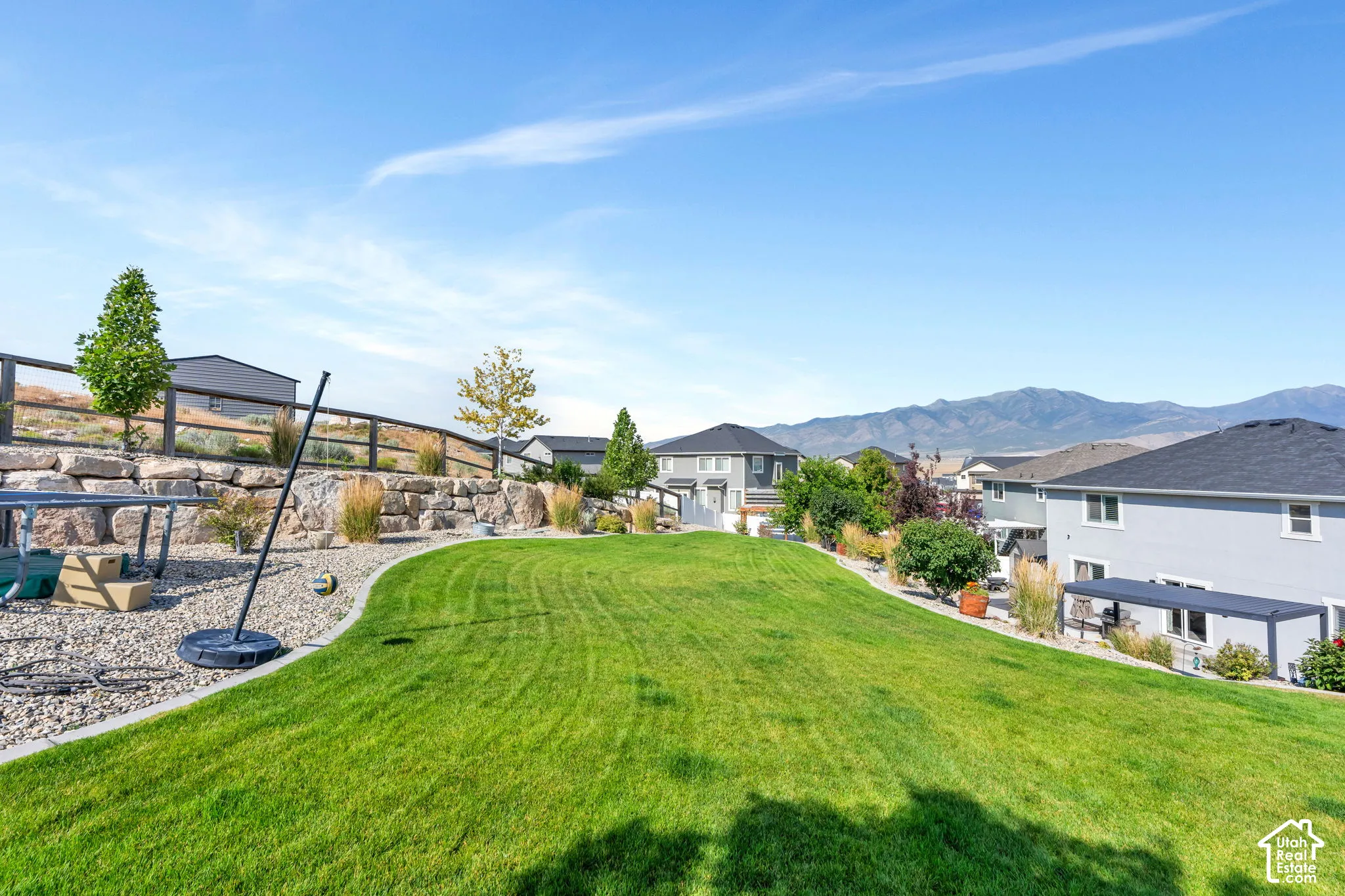 Expansive landscaped backyard featuring a manicured lawn, stone retaining wall, and mountain backdrop