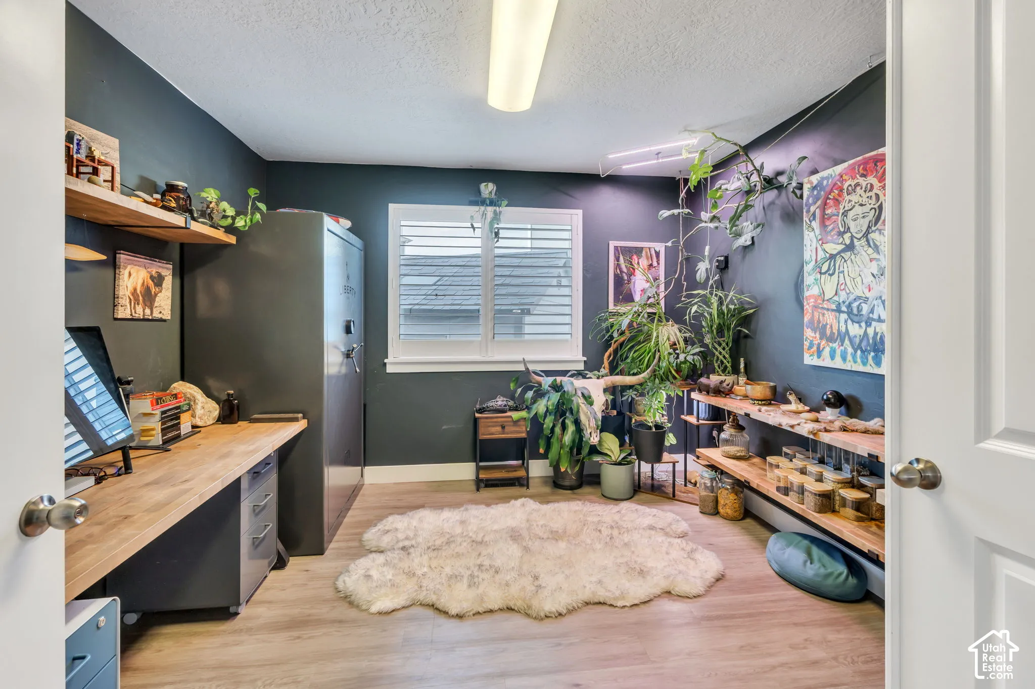 Light wood-finish flooring, built-in wooden shelving, and a window with white louvered shutters