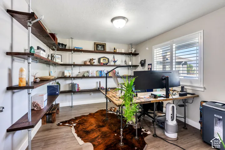 Built-in industrial-style shelving with wood-finish planks, wood-finish flooring, a window with plantation shutters, and an overhead flush-mount light fixture