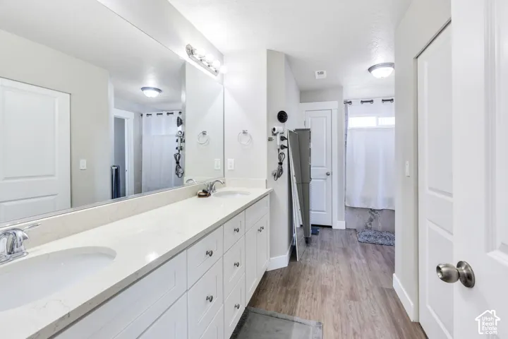 Dual under-mount sinks with chrome faucets, white cabinetry, a long vanity mirror, and wood-finish flooring