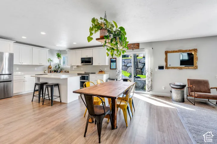 Kitchen with white cabinetry, stainless steel appliances, a center island with seating, and wood-finish flooring