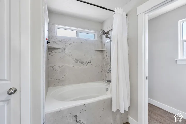 Alcove bathtub with a wall-mounted shower fixture, tiled surround, and integrated shelving