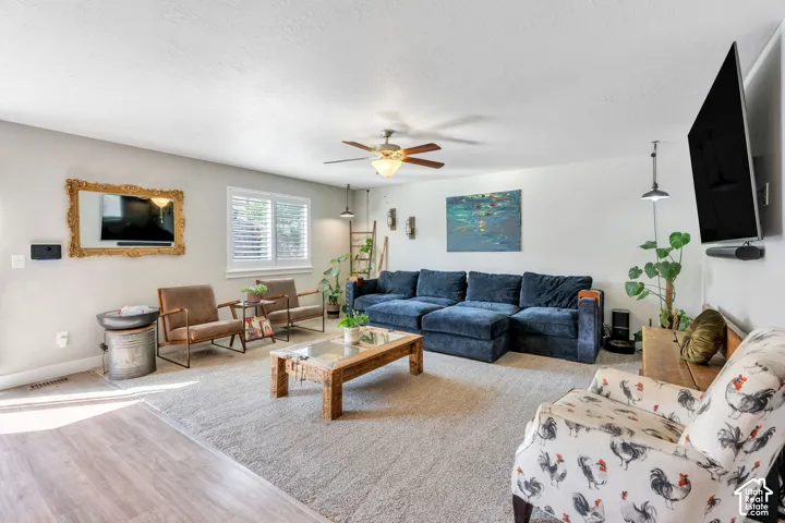 Spacious living area featuring wood-finish flooring, a ceiling fan, and window shutters