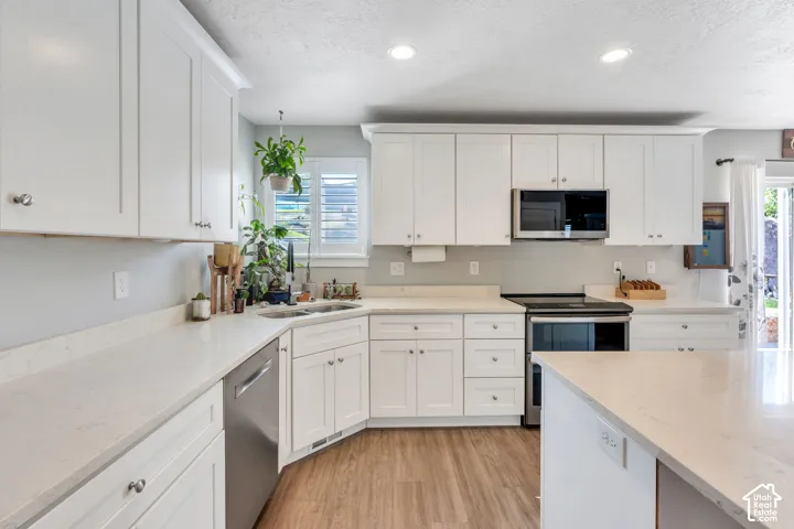 White cabinetry with silver hardware, light-toned countertops, stainless steel appliances, and wood-finish flooring