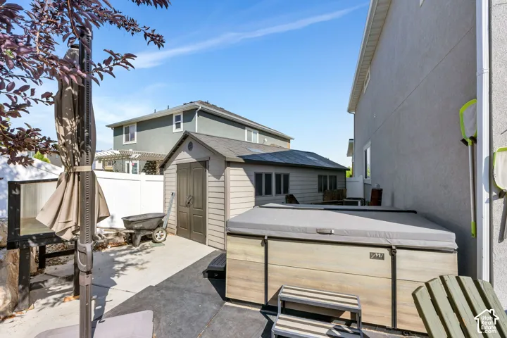 Outdoor concrete patio featuring a hot tub, storage shed, and white privacy fencing