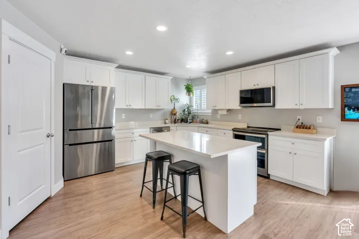 Modern kitchen featuring white cabinetry, light countertops, wood-finish flooring, a central island, and recessed lighting