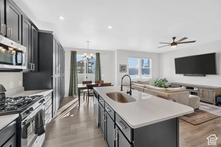 Open-concept living space featuring a kitchen with dark cabinetry, stainless steel appliances, a center island with an undermount sink, and wood-finish flooring throughout