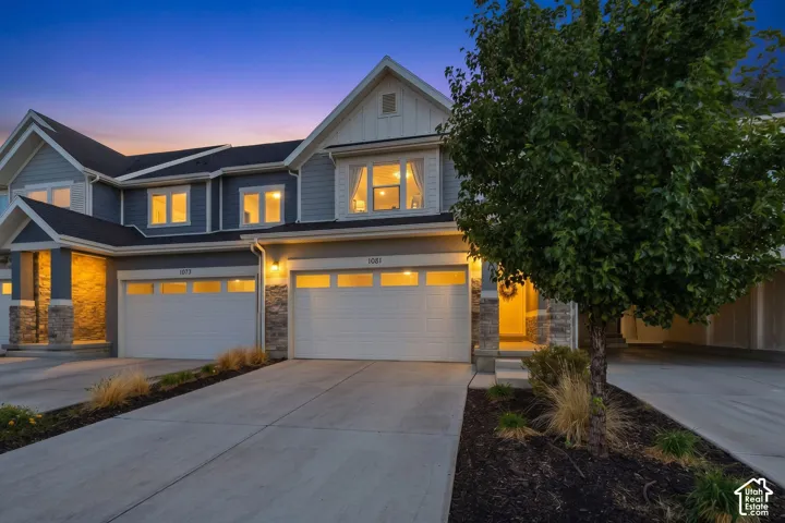 Multi-level residence featuring stone accents, white garage doors, and a concrete driveway