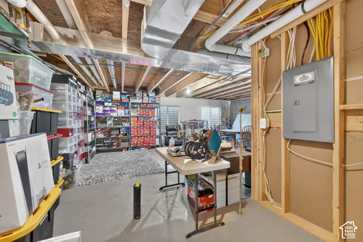 Unfinished basement with exposed ceiling joists and ductwork, concrete flooring, and a visible electrical panel